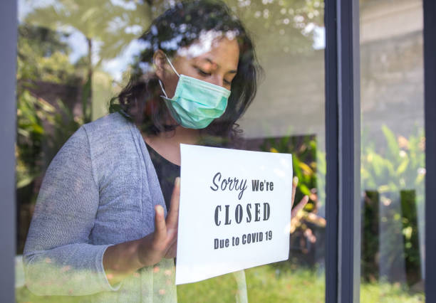 Asian entrepreneur closing business due to Covid 19 outbreak Portrait shot of an Asian restaurant owner putting a closing down poster into a door window due to Covid 19 outbreak lockdown business stock pictures, royalty-free photos & images