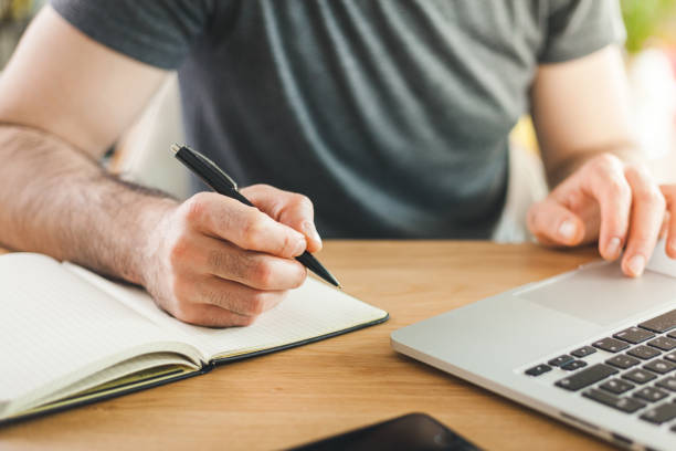 istock Man working on laptop and taking notes on a wooden table at home. 1220065910