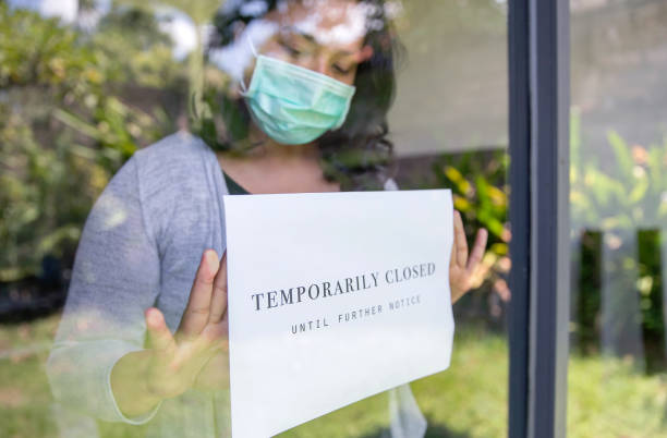 Business temporarily close due to Covid-19 outbreak Portrait shot of store business owner putting a temporarily closed sign at entrance door, during Covid 19 pandemic closed sign stock pictures, royalty-free photos & images