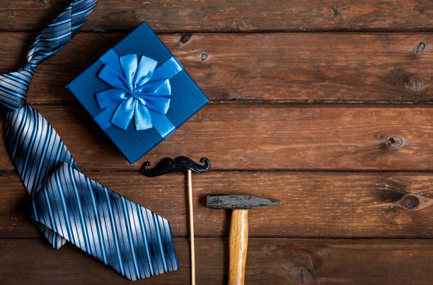istock Happy Fathers Day gift box with tie, hammer, blue box and mustache on a rustic wood background 1220071090