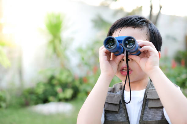 istock Curious little young Asian boy looking trough a blue binoculars in the garden. Exploring the world, outdoors activity 1220071232