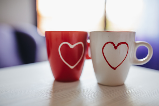 Two coffee cups with heart-shaped pattern stand at the table. Love concept objects