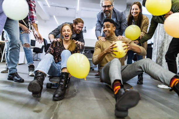 Cheerful freelancers having fun during skateboard competition at casual office. Large group of playful creative people having fun during skateboard race at casual office. race office stock pictures, royalty-free photos & images