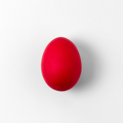One bright whole red chicken egg on a light background. Concept of a holiday or minimalistic geometric shapes