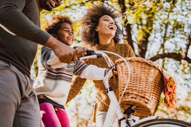 poniżej widok szczęśliwej czarnej dziewczyny na rowerze z rodzicami w naturze. - candid people casual bicycle zdjęcia i obrazy z banku zdjęć