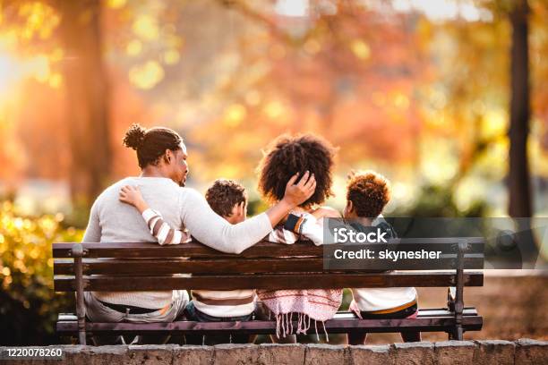 Back view of embraced black family in autumn day on a park bench.