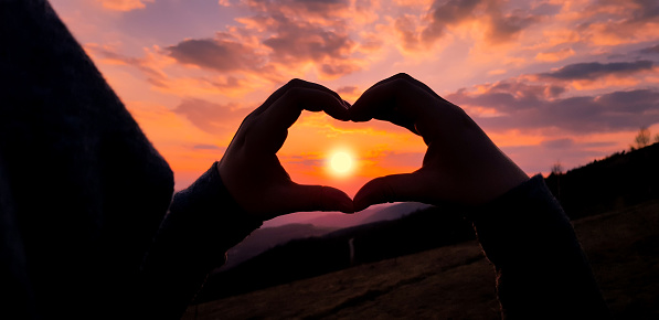 Very interesting detail. Heart shaped silhouette of woman's hands. Beautiful sunset in the background. The concept of an active and healthy life.