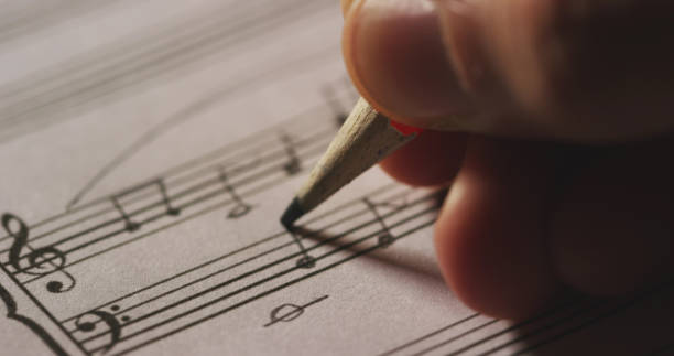 istock Macro close up of musician or composer hand writes a song or a musical work, writing notes with pencil on the pentagram 1220083046