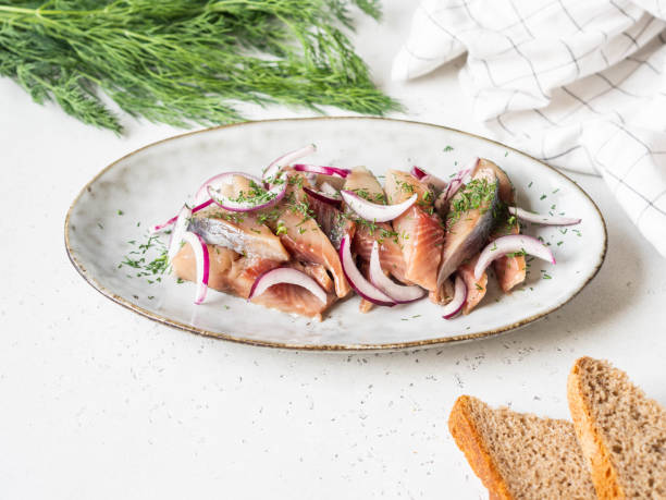 istock Marinated Herring fish slices with fresh dill and red onion, rye bread on the white table. 1220085172