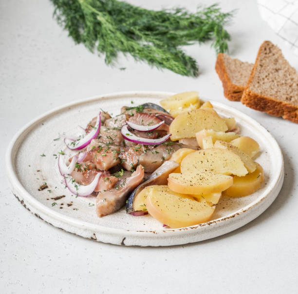 istock Marinated Herring fish with potatoes slices and red onion, rye bread on the white table. 1220085182