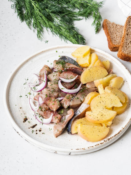 istock Marinated Herring fish with potatoes slices and red onion, rye bread on the white table. 1220085184