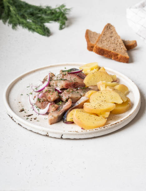 Marinated Herring fish with potatoes slices and red onion, rye bread on the white table.