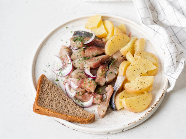 istock Marinated Herring fish with potatoes slices and red onion, rye bread on the white table. 1220085192