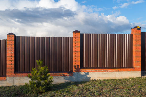 istock Pine near fence from corrugated board  with brick pillars in early spring 1220085960