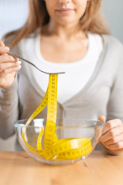 istock Young woman holding fork with measuring tapes. 1220086913