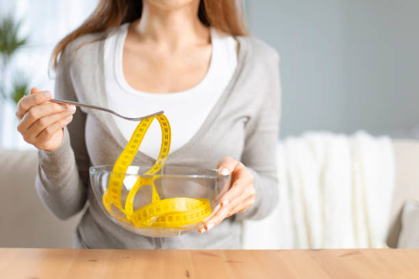 istock Young woman holding fork with measuring tapes. 1220086973
