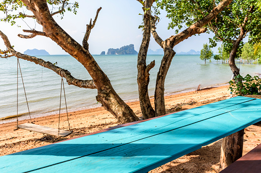 Covid-19 lockdown. Empty picnic table & wooden swing hangs from tree on deserted beach on Ko Yao Noi island in Phang-Nga Bay near Phuket, Thailand