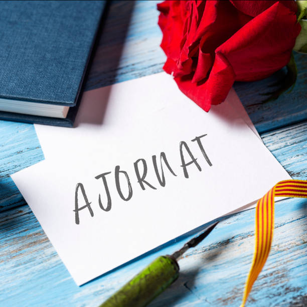 istock red rose, book and text postponed in Catalan 1220089082