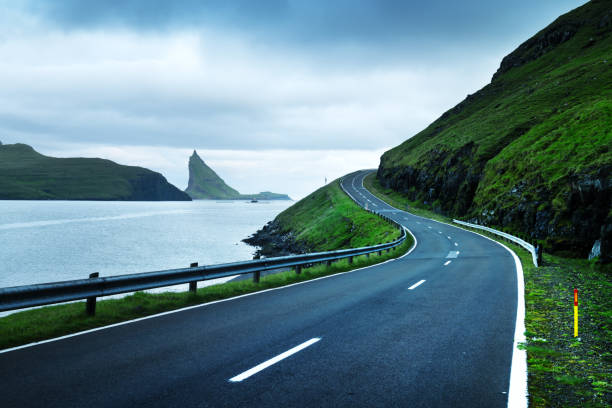 Dramatic evening view of road and Tindholmur cliffs Dramatic evening view of the road and the Drangarnir and Tindholmur rocks in the background on the island of Vagar, Faroe Islands, Denmark vágar photos stock pictures, royalty-free photos & images