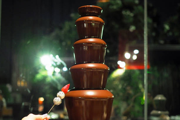 istock Picking fruit skewer stick into chocolate fountain fondue placed on a table in hotel restaurant. 1220089973