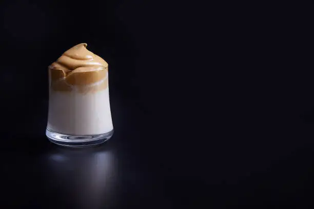 Iced Korean Dalgona-Coffee, a trendy fluffy creamy whipped coffee on a black background. Copy space