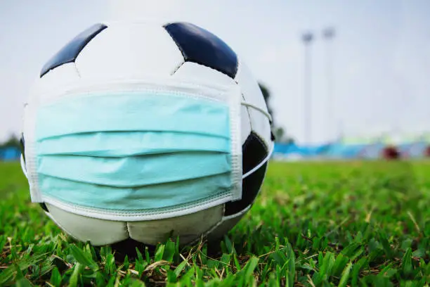 Photo of soccer ball with medical mask in the empty stadium. covid-19 spreading outbreak