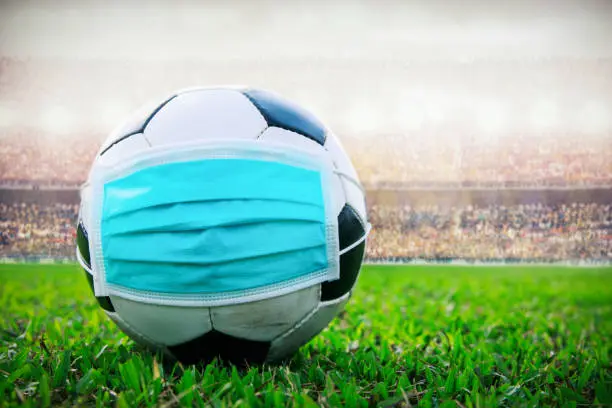 Photo of soccer ball with medical mask in the stadium. All event of soccer pause break. covid-19 spreading outbreak