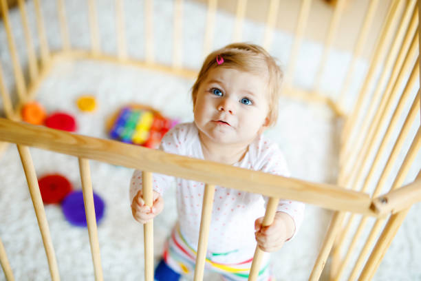 mooi klein babymeisje dat zich binnen box bevindt. leuk aanbiddelijk kind dat met kleurrijk speelgoed speelt. thuis of kinderdagverblijf, veiligheid voor kinderen. alleen baby die op mamma wacht - babybox stockfoto's en -beelden