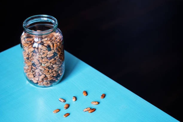 istock Pinto beans in a glass jar with grains on the table on a black background with empty space on the left. Minimalist style shot 1220097625