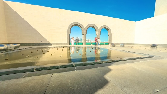 Doha, Qatar - February 20, 2019:TIME LAPSE of courtyard of Museum of Islamic Art with arched windows opening view on Doha West Bay skyline and Persian Gulf. Tourists visit the popular museum.