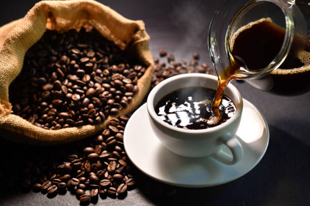 istock Pouring coffee with smoke on a cup and coffee beans on burlap sack on black background 1220101953