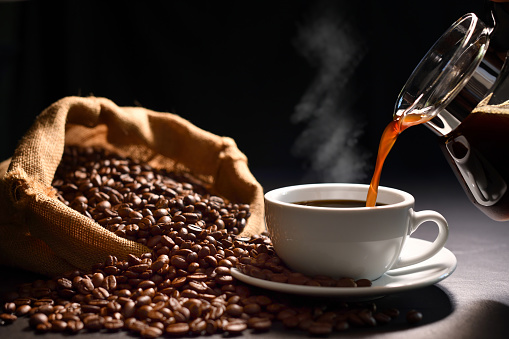 Pouring coffee with smoke on a cup and coffee beans on burlap sack on black background photo
