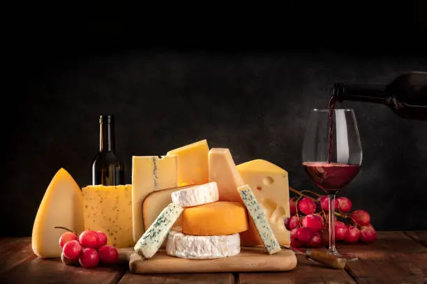 Photo of Cheeses with grapes and pouring wine, a side view on a dark background with copy space