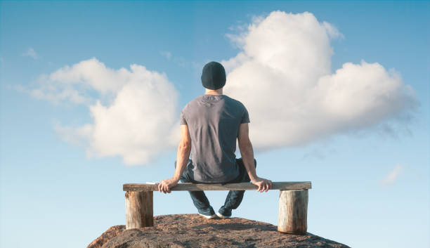 istock A man sits on a wooden bench on top of a cliff. Back view. 1220104240
