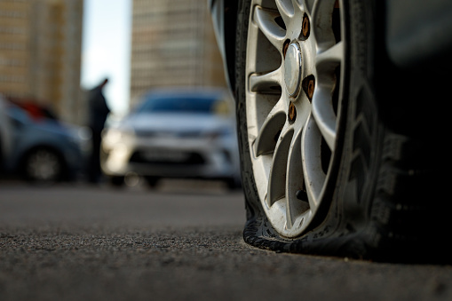 Car tire with a flat tire in the yard near a multi-storey building. Image of an accident, damage, breakdown for illustration on the topic of repair, insurance. Close-up, blurred