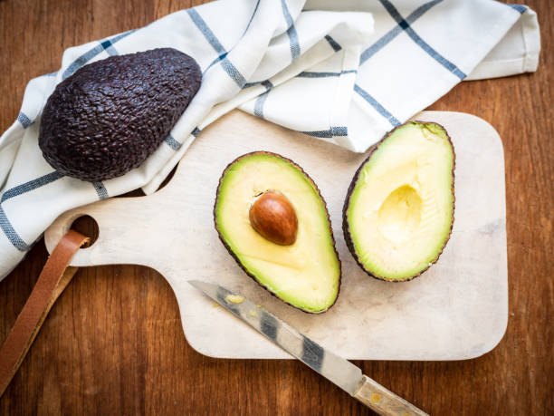 istock Two halves of avocado with a core on a cutting board and a checkered kitchen towel on a rustic table 1220108680