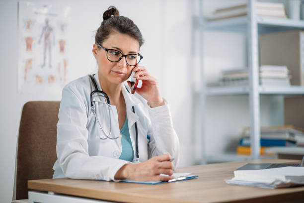 Female doctor taking a call from a patient during quarantine. Prescribing therapy from a remote medical office to isolated patient. Female doctor taking a call from a patient during quarantine curfew stock pictures, royalty-free photos & images