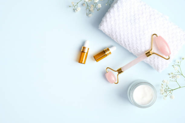 istock Jade face roller with moisturizer cream and essential oil on blue background. Flat lay, top view. Massage tool for facial skin care, SPA beauty treatment concept 1220114532