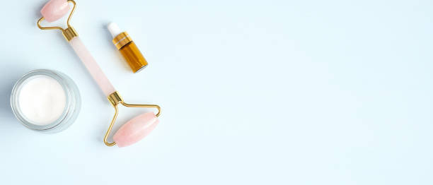 istock Rose quartz face roller with moisturizer cream and essential oil on blue background. Flat lay, top view. Massage tool for facial skin care, SPA beauty treatment concept 1220114541