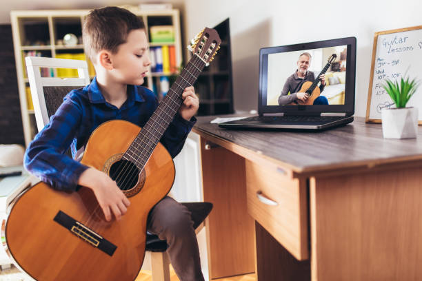 istock Happy little boy learning to play guitar while watching lessons at laptop at home 1220120533