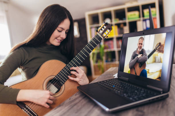 istock Happy little girl learning to play guitar while watching lessons at laptop at home 1220121321