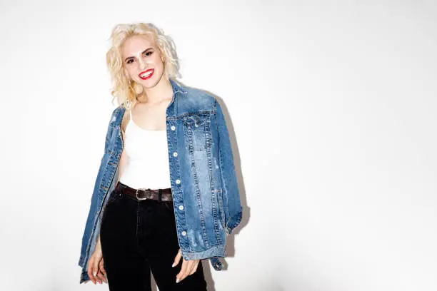 happy smiling young blonde girl in a white T-shirt and denim jacket on a white background, studio fashion photo with copy space