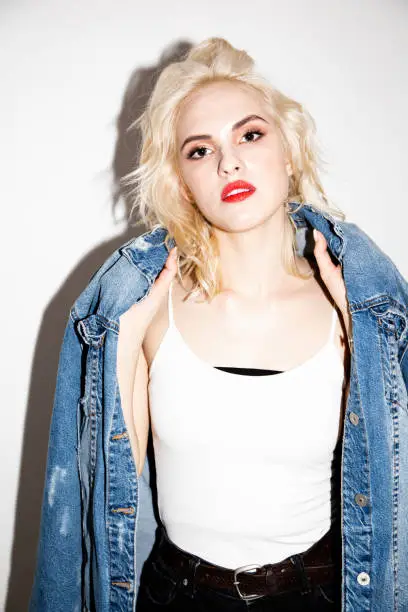 sexy lovely young blonde girl in a white T-shirt and denim jacket on a white background, studio fashion photo