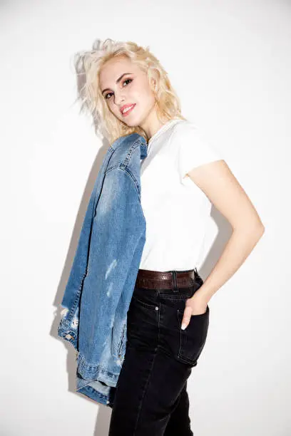 happy young blonde girl in a white T-shirt and denim jacket on a white background, studio fashion photo
