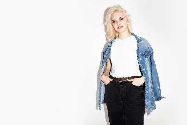 happy young blonde girl in a white T-shirt and denim jacket on a white background, studio fashion photo with copy space