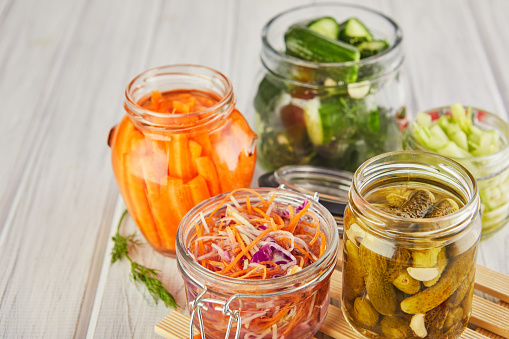 Fermented preserved vegetarian food concept. Sour sauerkraut, pickled carrots, pickled cucumbers, pickled celery in glass jars on a white wooden kitchen table. The concept of canned food. Copy space