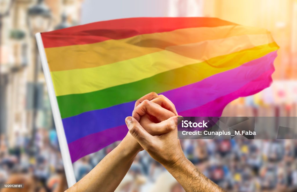 paar dat handen en golf voor een regenboogvlag houdt - Royalty-free Pride - LGBTQI-evenement Stockfoto