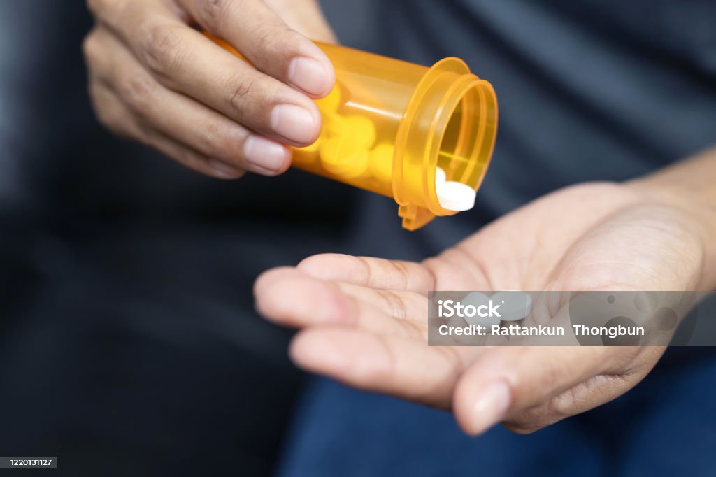Woman hand with pills on, spilling pills out of bottle on dark background. Opioid Stock Photo