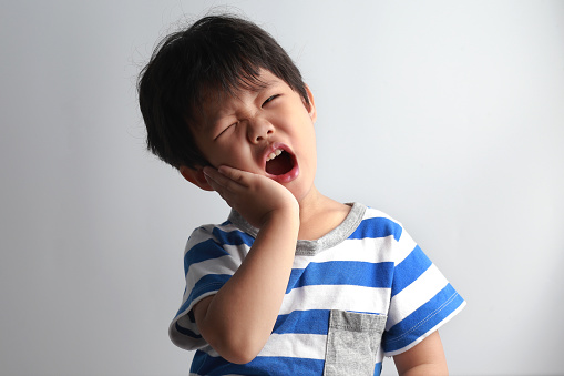 Little Asian boy having toothache, holding his face with hand, dental problem.