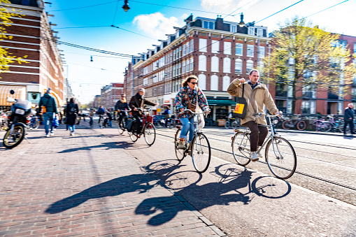 A street during a bright spring day in Amsterdam, Netherlands with cyclists going along a cycle lane.